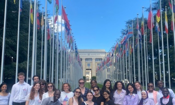 Quaker United Nations Summer School 2023 participants at their visit to the United Nations in Geneva; group photo in front of the flags