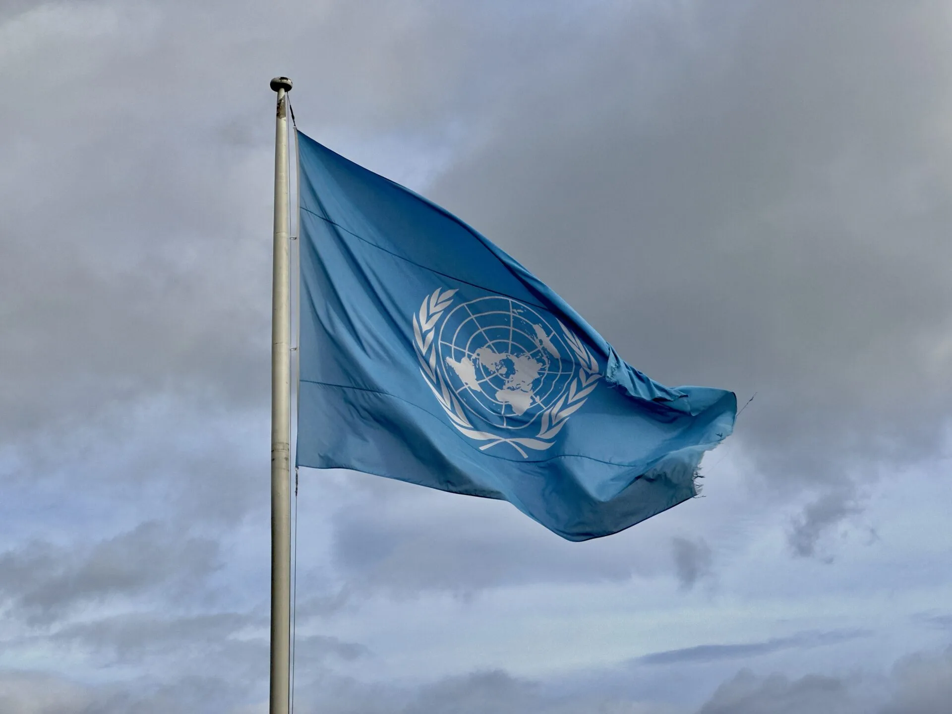 United_Nations_UN_flag_(FN-flagget)_waving_on_flagpole._Heavy_clouds._ARKIVET_Peace_and_Human_Rights_Centre._Vesterveien_4,_Bellevue,_Kristiansand_NORWAY_2023-10-17_IMG_3723